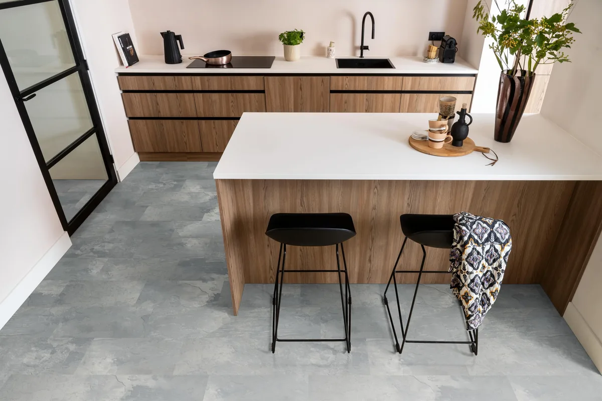 Madison Square Aqua / Expression Aqua middengrijs, tegellaminaat met natuursteenlook in een keuken met een houten kookeiland en zwarte barkrukken