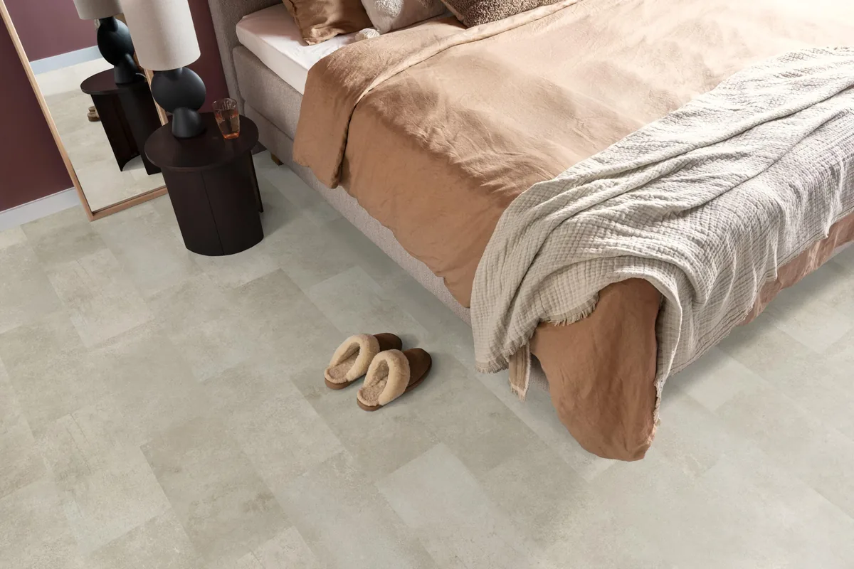 Madison Square Aqua / Expression Aqua grijsbruin, tegellaminaat met natuursteenlook in een slaapkamer, met sloffen naast het bed en een donker nachtkastje