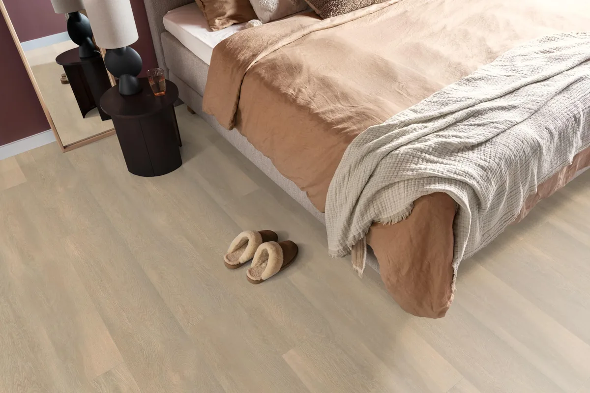 East Village / Arnstadt natuur eiken, laminaat in een slaapkamer, met sloffen naast het bed en een donker nachtkastje