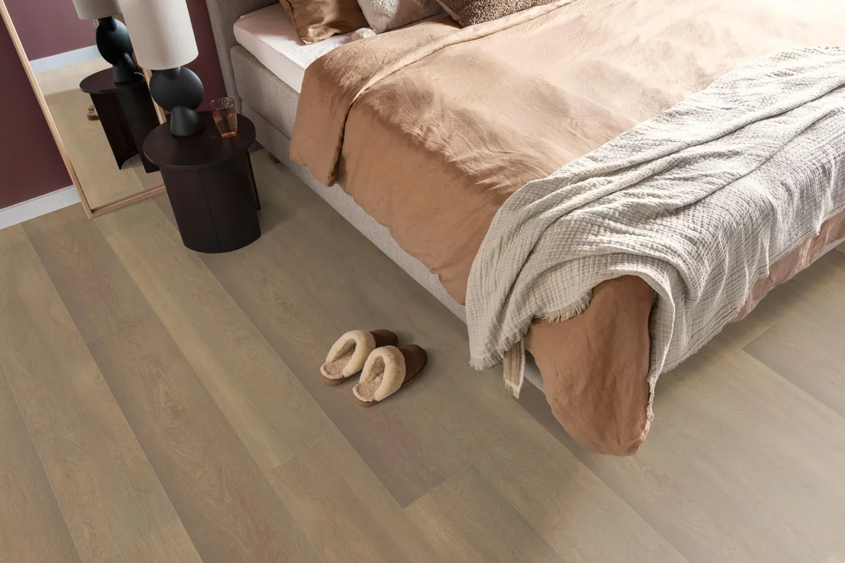 East Village / Arnstadt smoky eiken, laminaat in een slaapkamer, met sloffen naast het bed en een donker nachtkastje