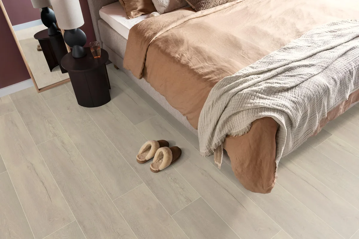 Union Square / Saarland wit eiken, laminaat in een slaapkamer, met sloffen naast het bed en een donker nachtkastje