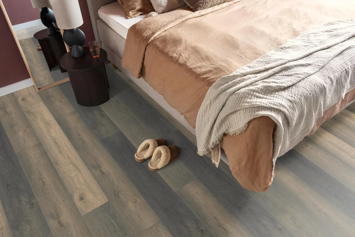 Midwood / Saksen titan eiken, laminaat in een slaapkamer, met sloffen naast het bed en een donker nachtkastje