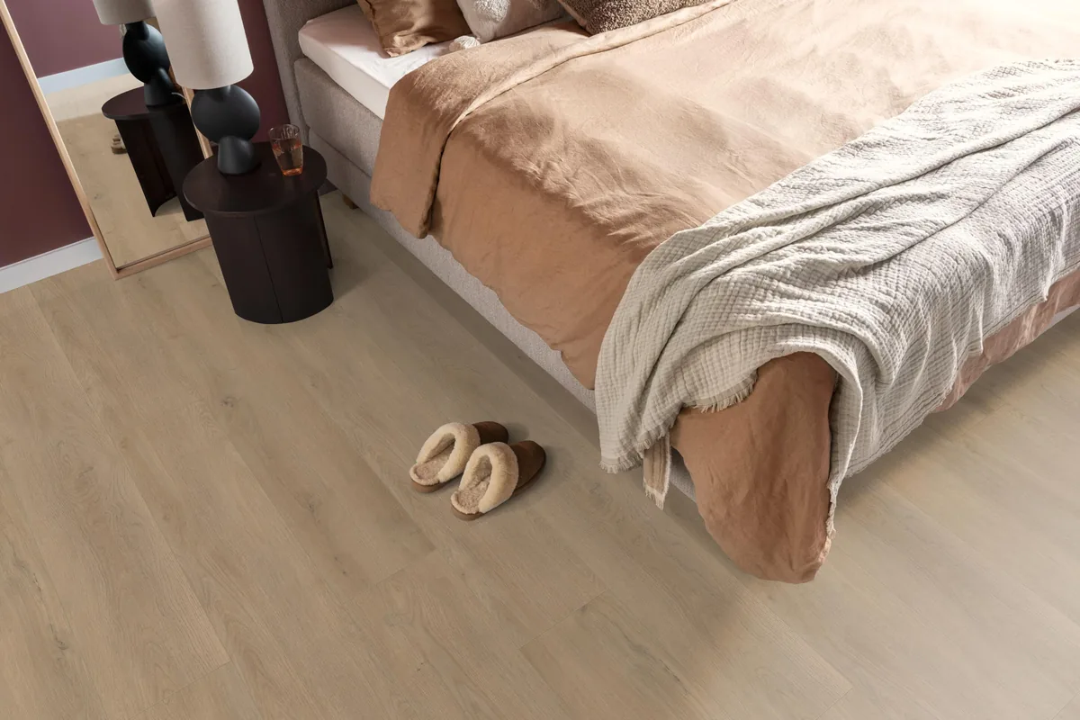 Marble Hill / Sereno warm eiken, laminaat in een slaapkamer, met sloffen naast het bed en een donker nachtkastje