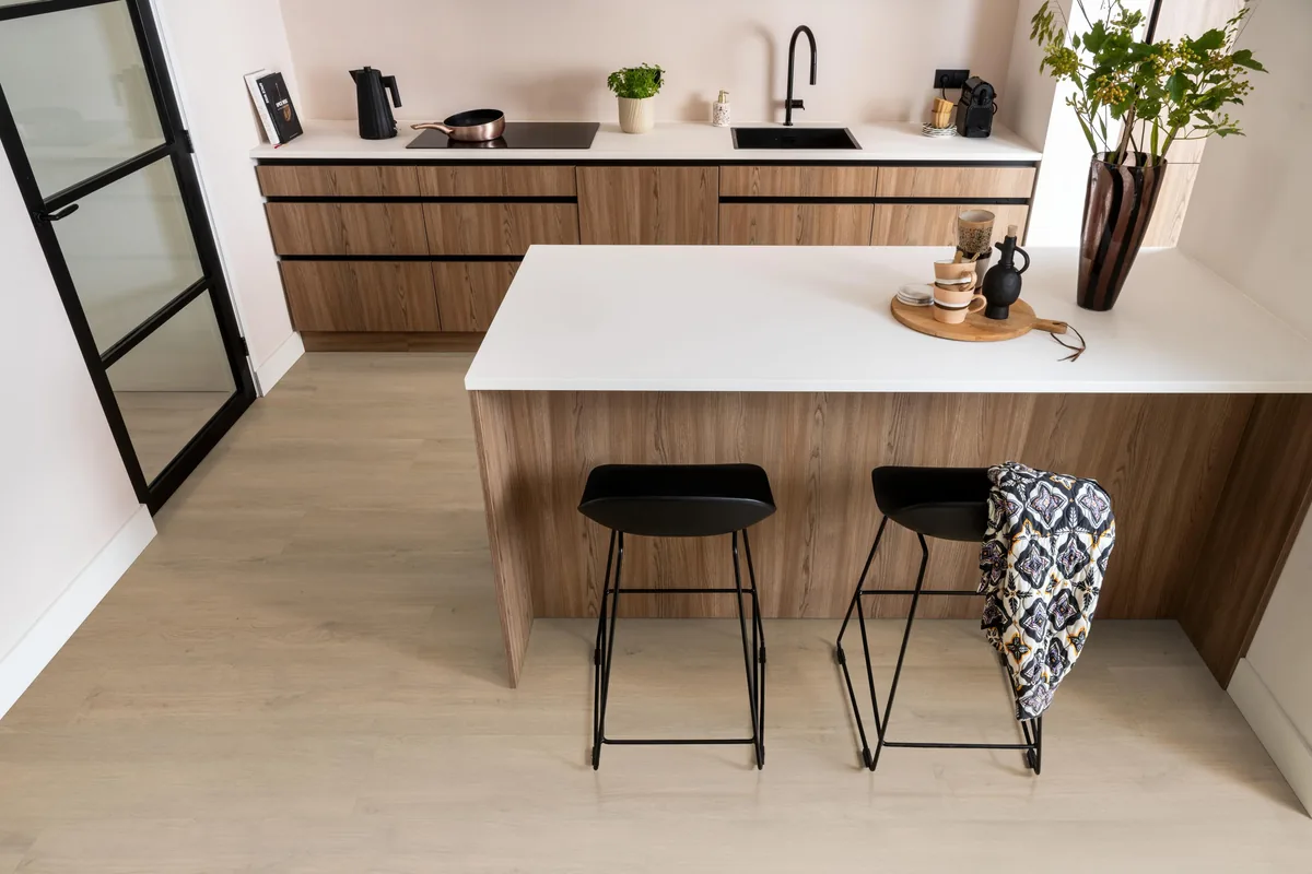 Marble Hill / Sereno warm eiken, laminaat in een keuken met een houten kookeiland en zwarte barkrukken