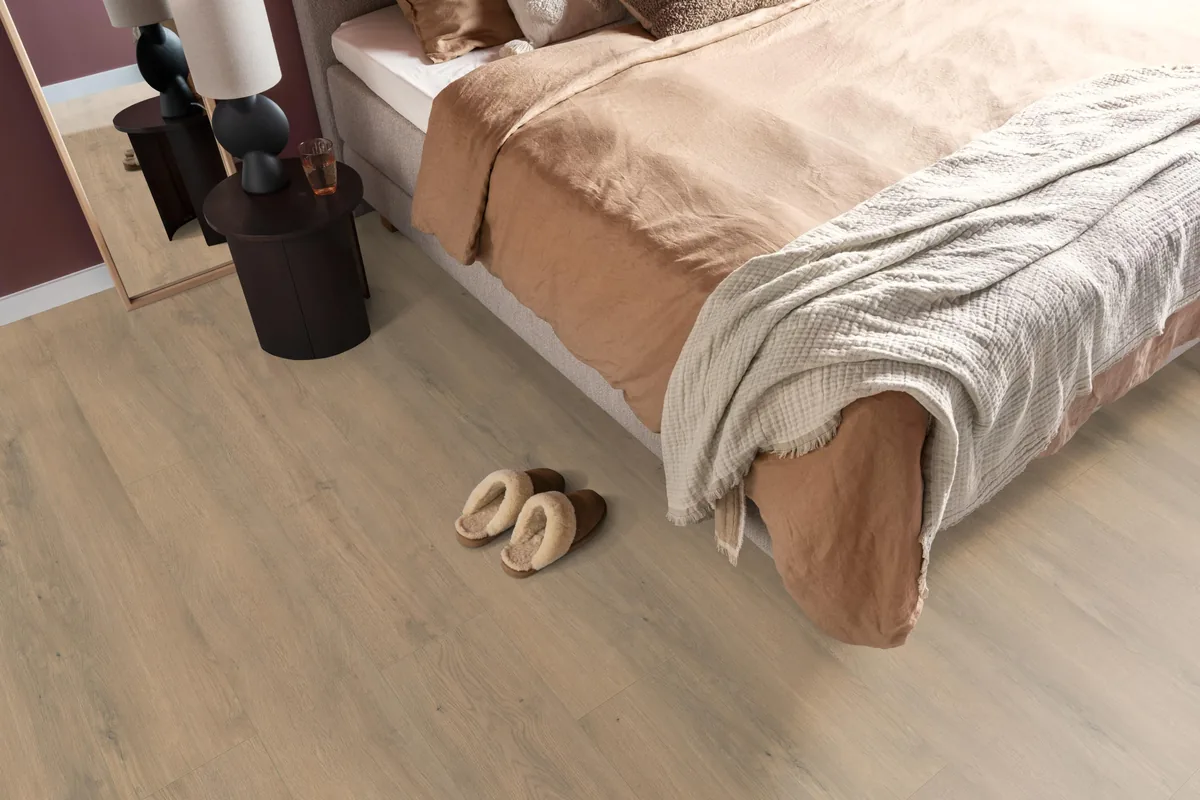 Marble Hill / Sereno beige eiken, laminaat in een slaapkamer, met sloffen naast het bed en een donker nachtkastje