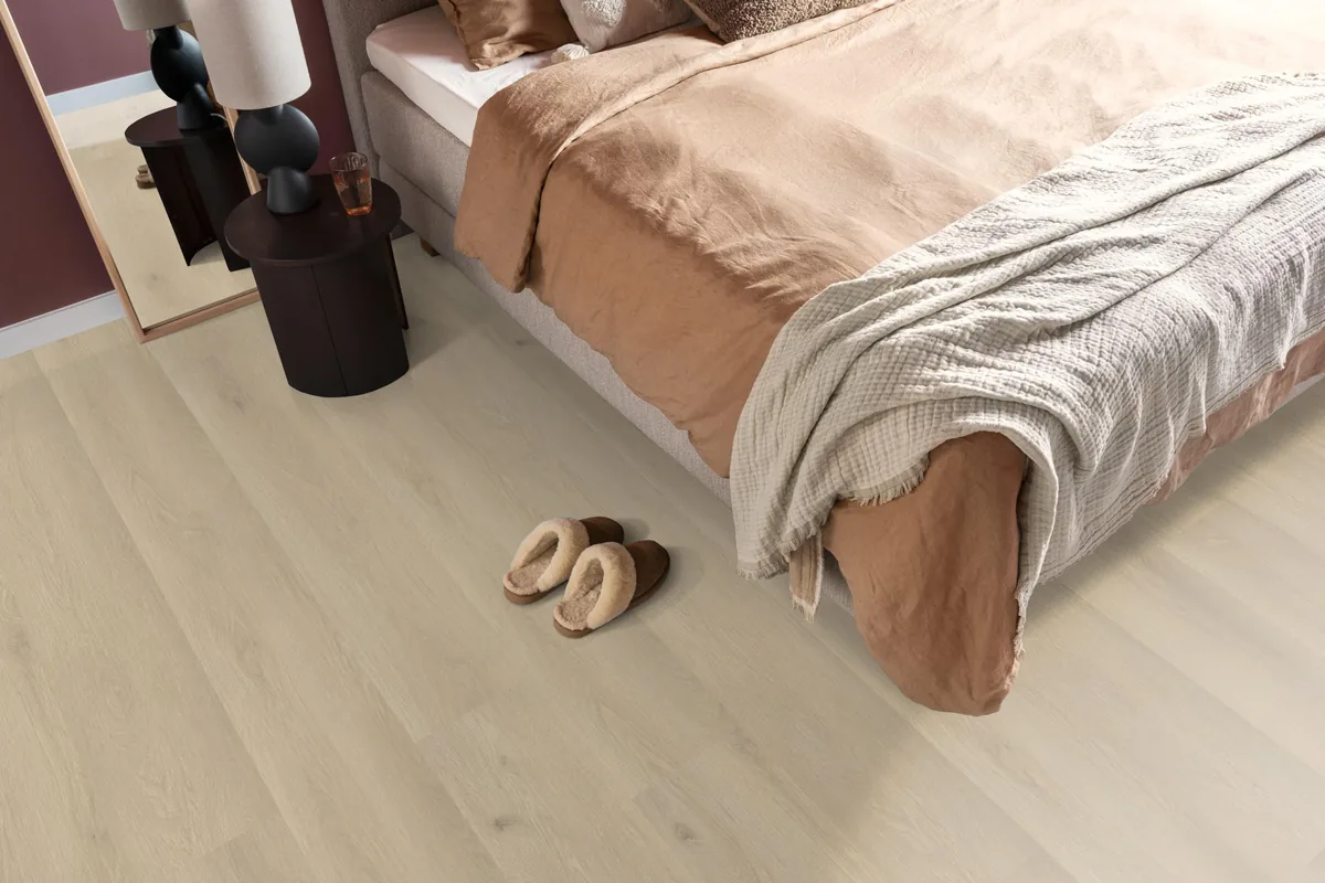 Gramercy Square / Marano beige eiken, laminaat in een slaapkamer, met sloffen naast het bed en een donker nachtkastje