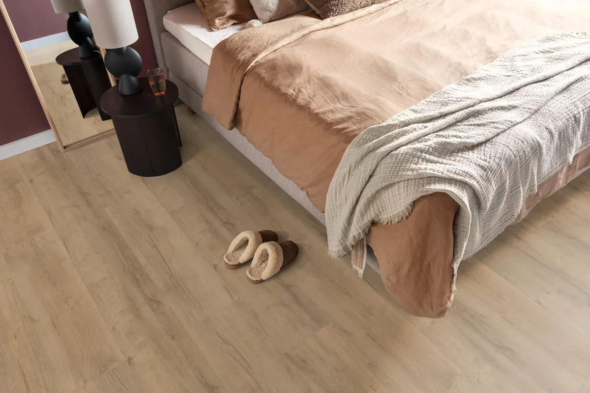 Sunnyside / Superior oak licht eiken, laminaat in een slaapkamer, met sloffen naast het bed en een donker nachtkastje