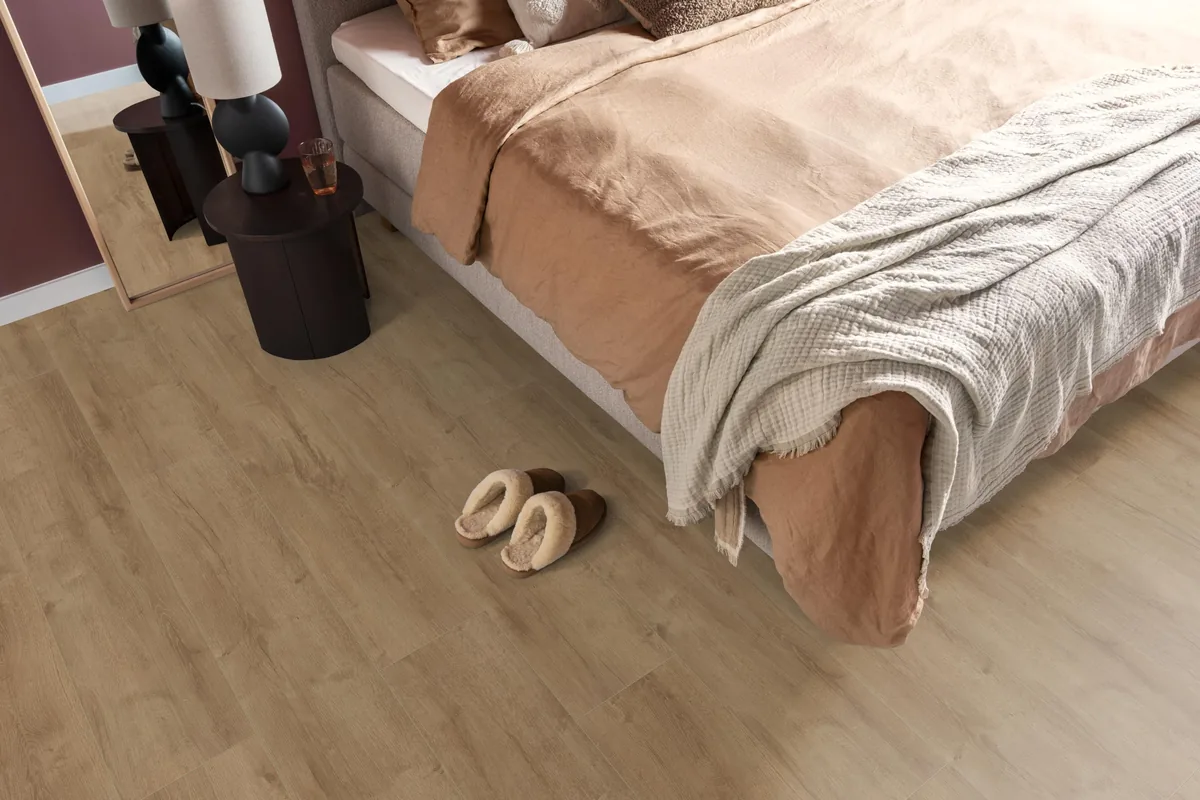 Sunnyside / Superior oak lichtbruin eiken, laminaat in een slaapkamer, met sloffen naast het bed en een donker nachtkastje