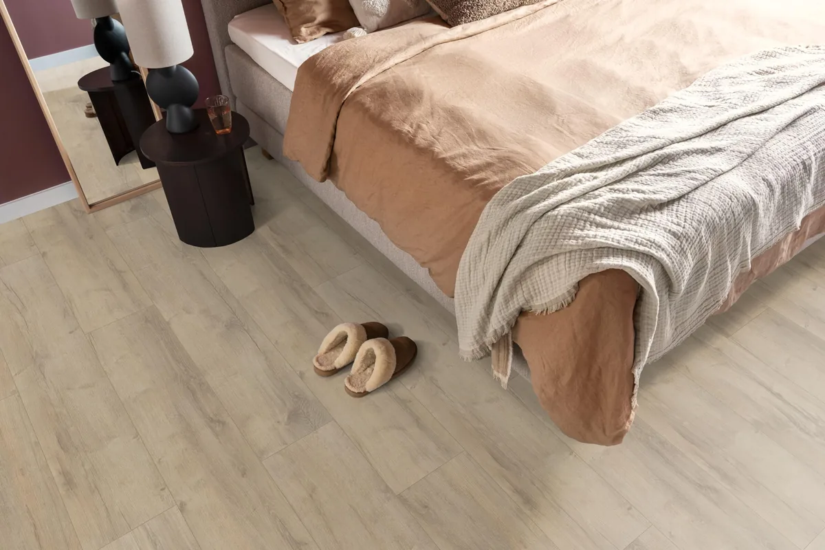Sunnyside / Superior oak beige eiken, laminaat in een slaapkamer, met sloffen naast het bed en een donker nachtkastje