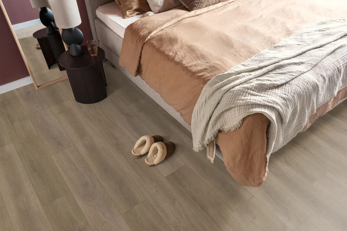 Woodside / Sunny oak smoky eiken, laminaat in een slaapkamer, met sloffen naast het bed en een donker nachtkastje