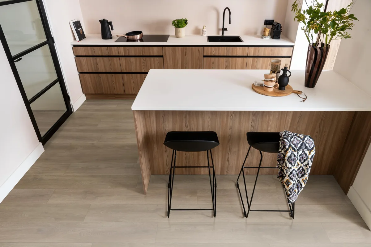 Woodside / Sunny oak smoky eiken, laminaat in een keuken met een houten kookeiland en zwarte barkrukken