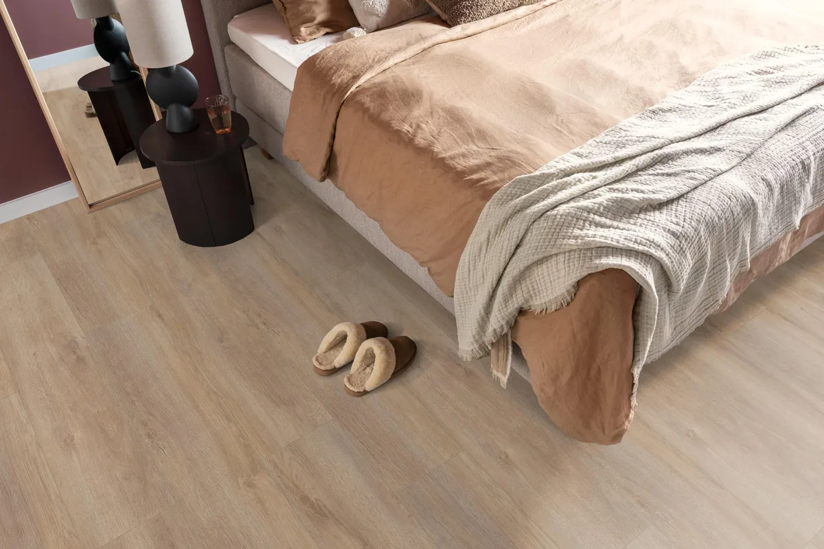 Norwood / Prestige oak warm eiken, laminaat in een slaapkamer, met sloffen naast het bed en een donker nachtkastje