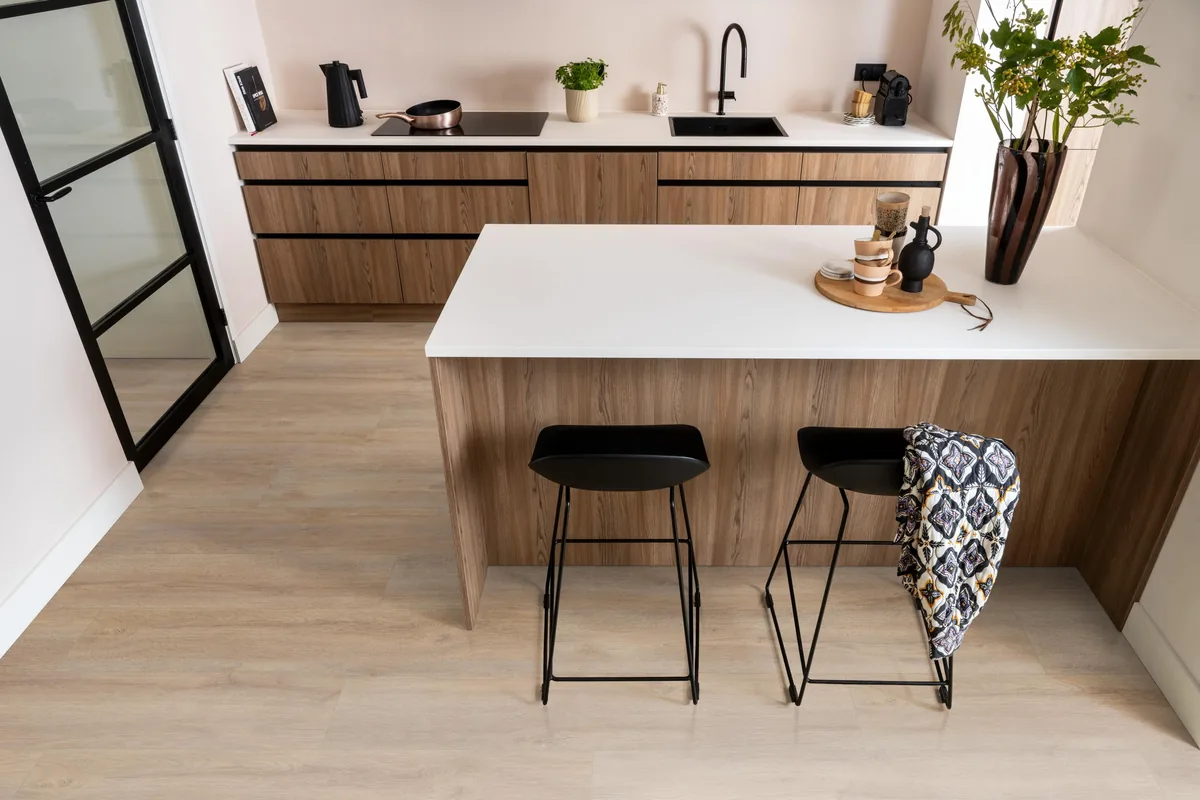 Norwood / Prestige oak warm eiken, laminaat in een keuken met een houten kookeiland en zwarte barkrukken
