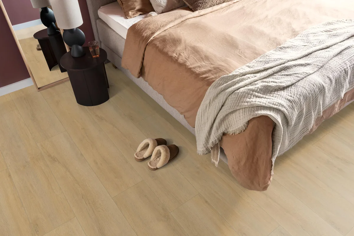 Norwood / Prestige oak natuur eiken, laminaat in een slaapkamer, met sloffen naast het bed en een donker nachtkastje