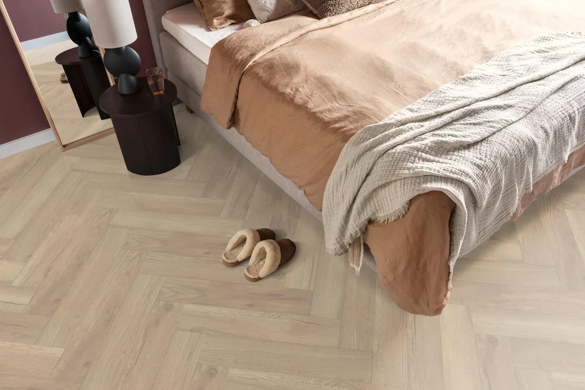 Bayside / Marquant eiken licht naturel, visgraat laminaat in een slaapkamer, met sloffen naast het bed en een donker nachtkastje