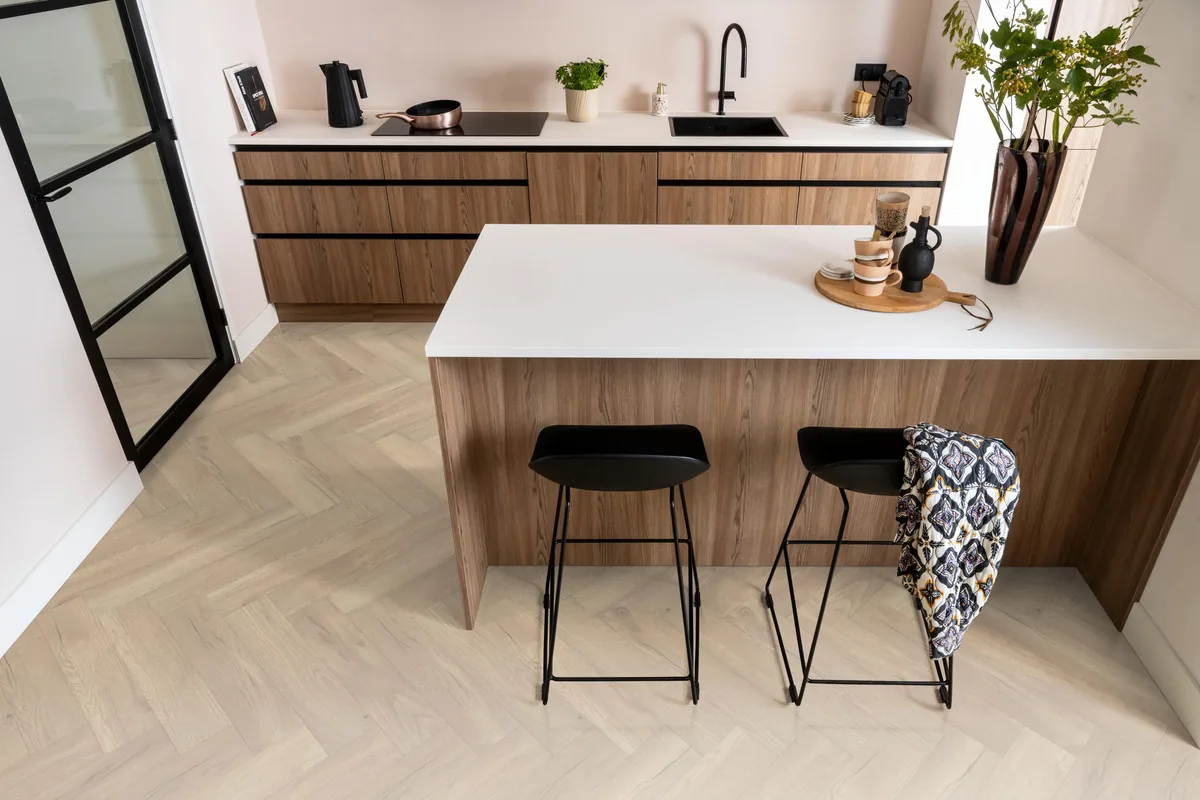 Bayside / Marquant eiken licht naturel, visgraat laminaat in een keuken met een houten kookeiland en zwarte barkrukken
