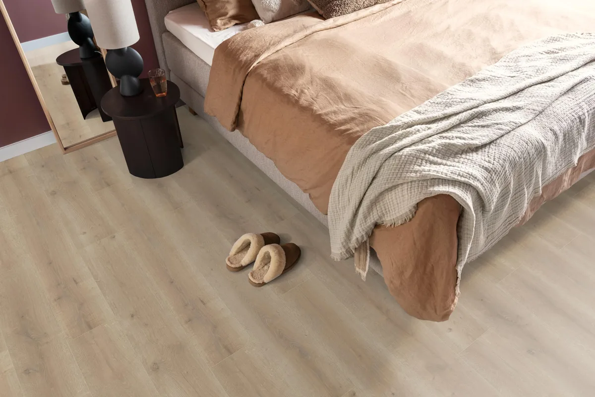 Queens / Elite naturel eiken, laminaat in een slaapkamer, met sloffen naast het bed en een donker nachtkastje