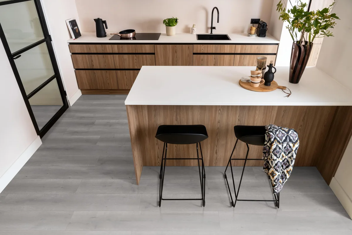 Queens / Elite grijs eiken, laminaat in een keuken met een houten kookeiland en zwarte barkrukken