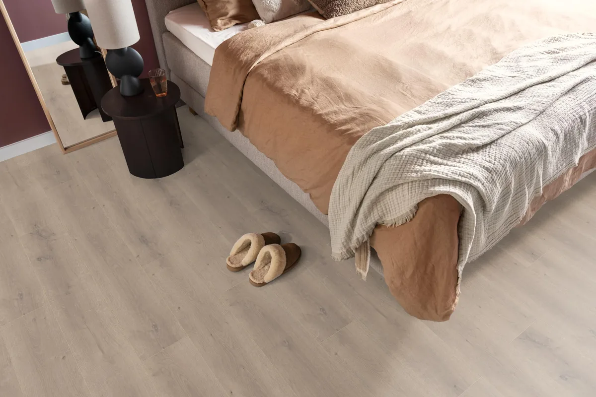 Queens / Elite beige eiken, laminaat in een slaapkamer, met sloffen naast het bed en een donker nachtkastje
