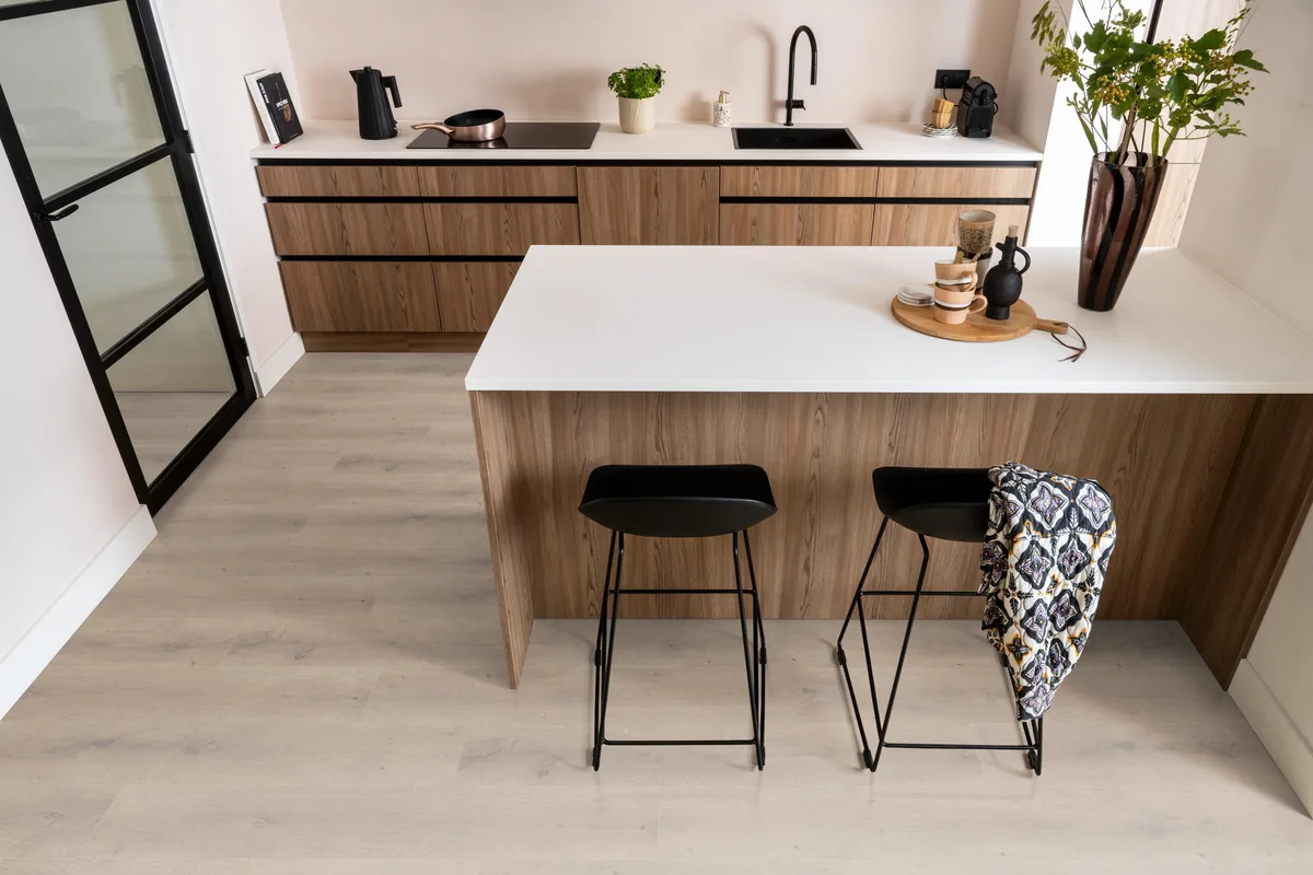 Queens / Elite beige eiken, laminaat in een keuken met een houten kookeiland en zwarte barkrukken