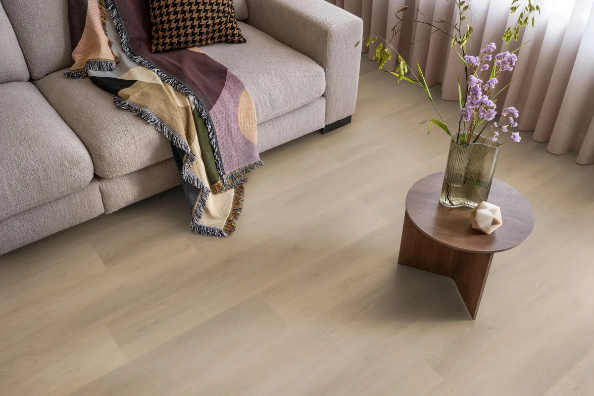 Newham / Sentima Beige, klik pvc in een woonkamer, met een beige bank en een ronde bijzettafel met bloemen