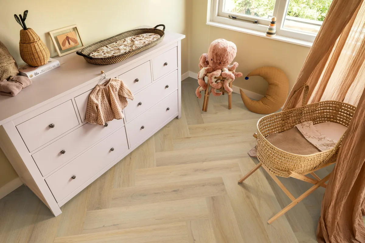 Greenford / Valento Natural, visgraat plak pvc in een babykamer, met een witte commode en een rieten wieg