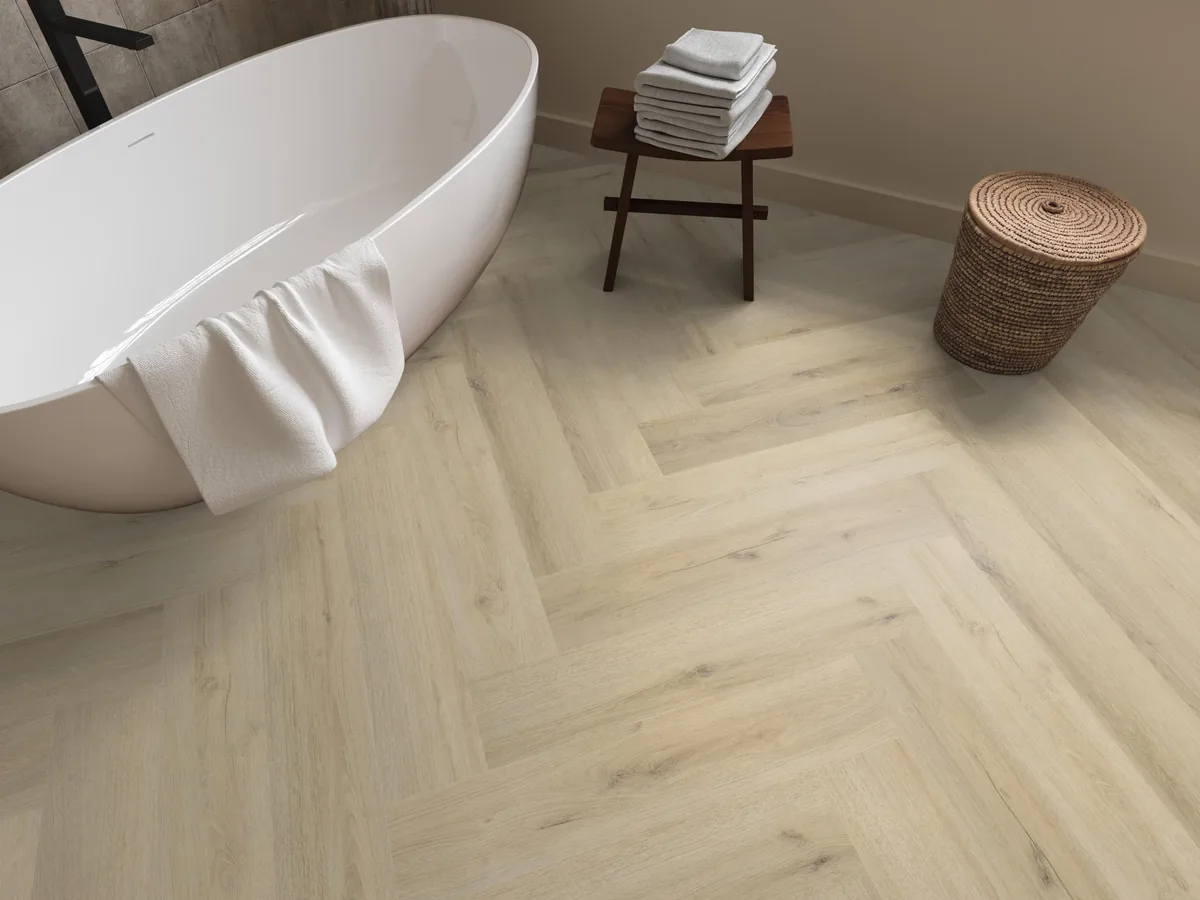 Greenford / Valento Warm beige, visgraat plak pvc in een badkamer, met een vrijstaand bad en een rieten wasmand