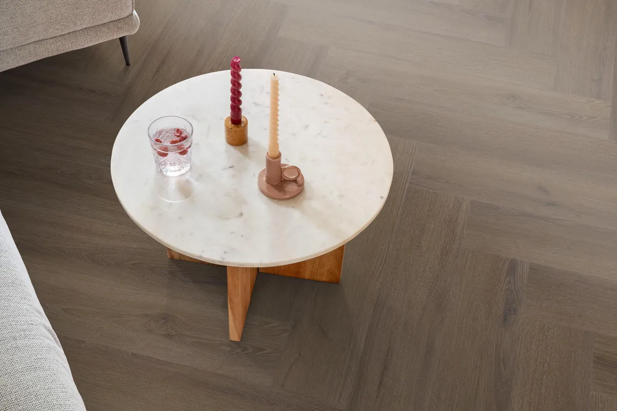 Greenford / Valento Brown, visgraat plak pvc in een woonkamer, met een ronde marmeren salontafel en twee kaarsen