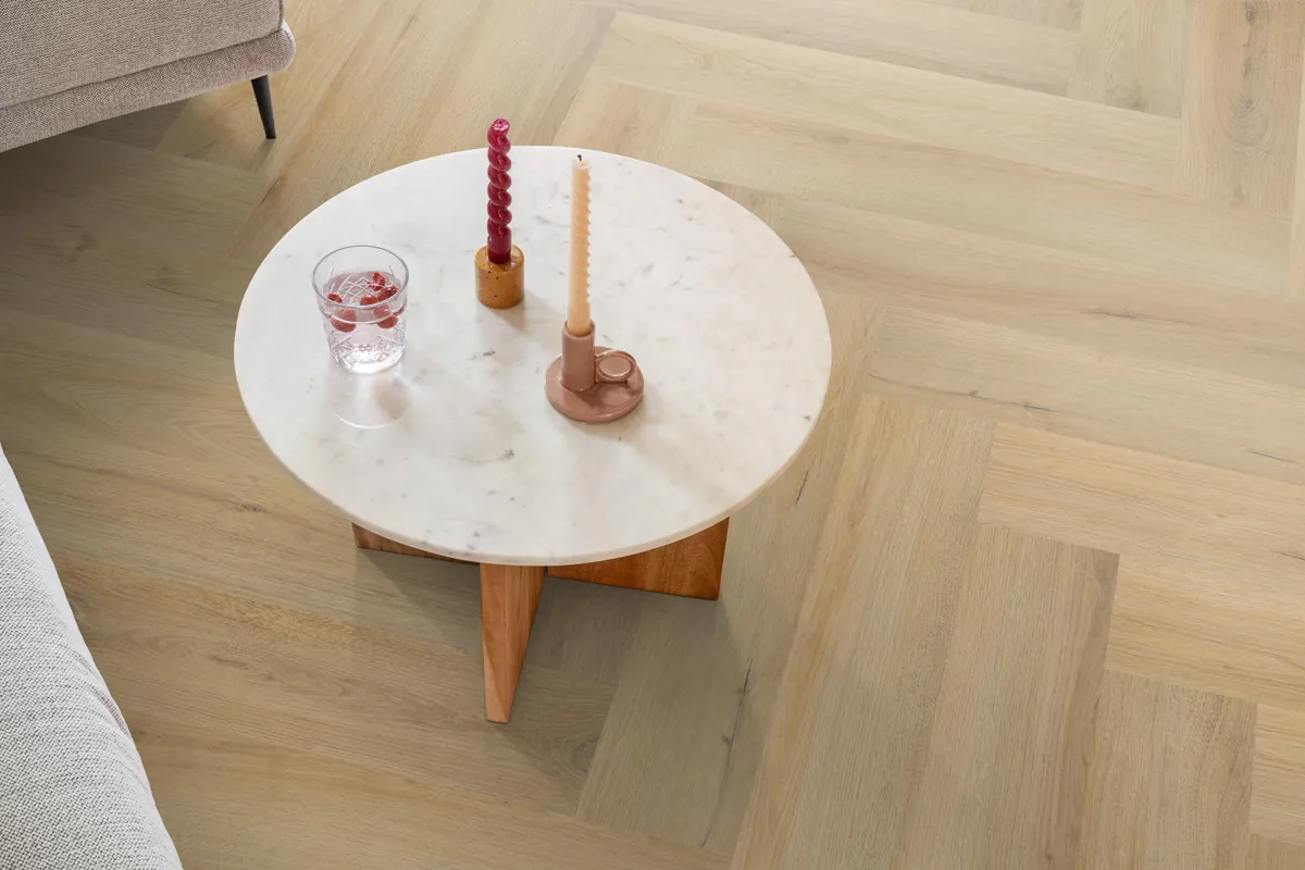 Greenford / Valento Natural, visgraat klik pvc in een woonkamer, met een ronde marmeren salontafel en twee kaarsen
