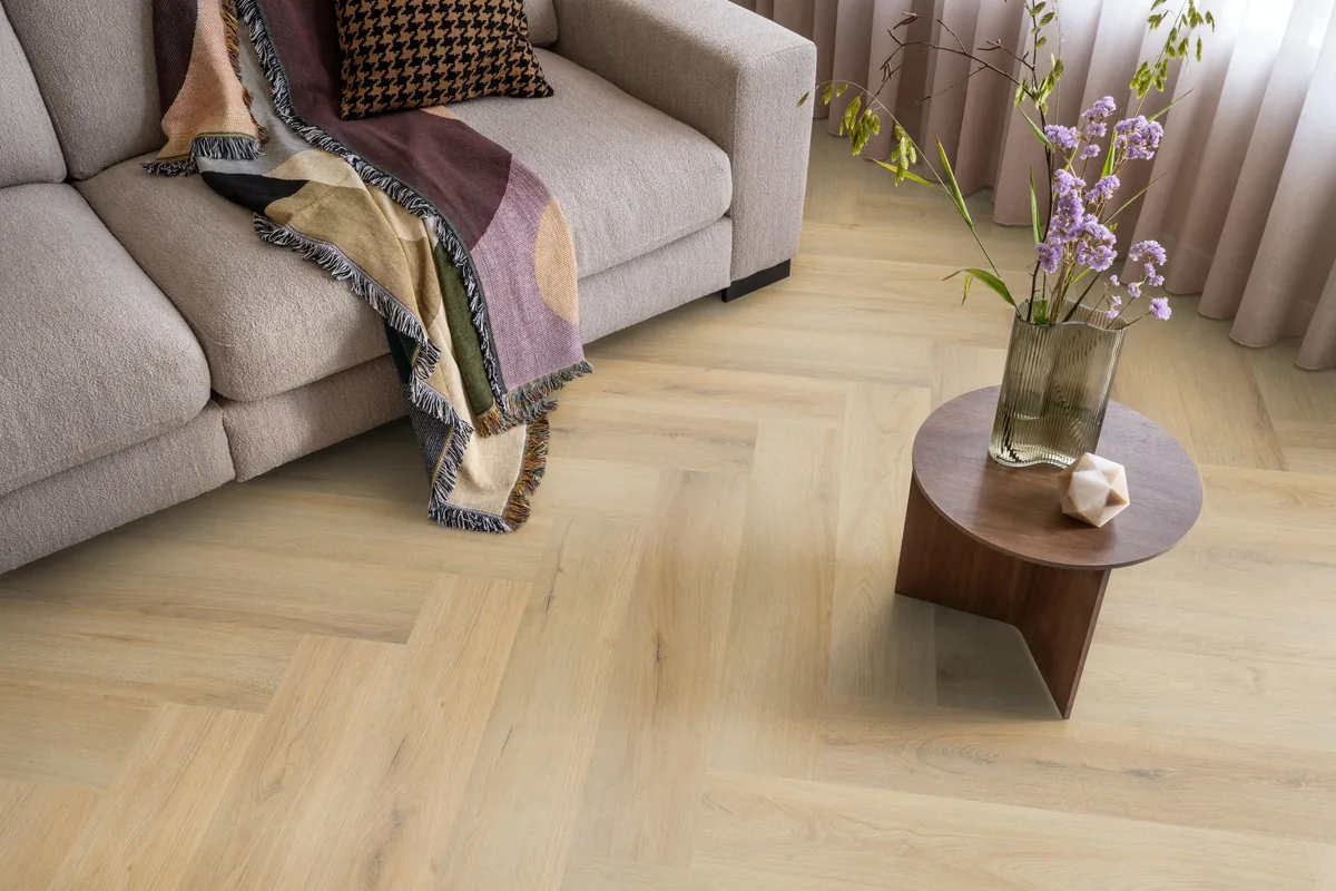 Greenford / Valento Natural, visgraat klik pvc in een woonkamer, met een beige bank en een ronde bijzettafel met bloemen