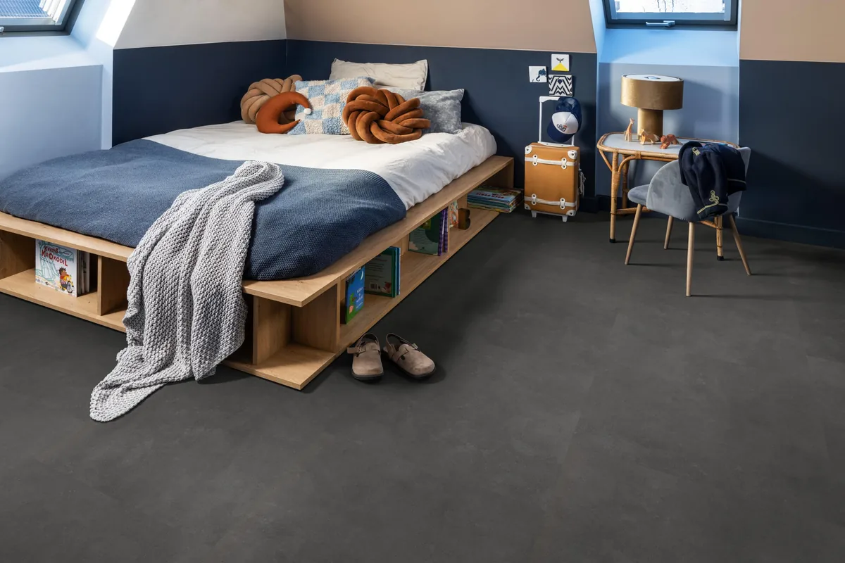 Victoria / Ceramo anthracite, plak pvc in een slaapkamer onder een schuin dak, met een houten bedombouw en sloffen ervoor