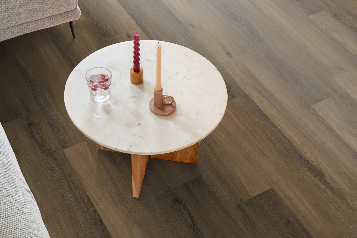 Paddington / Avanto Warm brown, klik pvc in een woonkamer, met een ronde marmeren salontafel en twee kaarsen