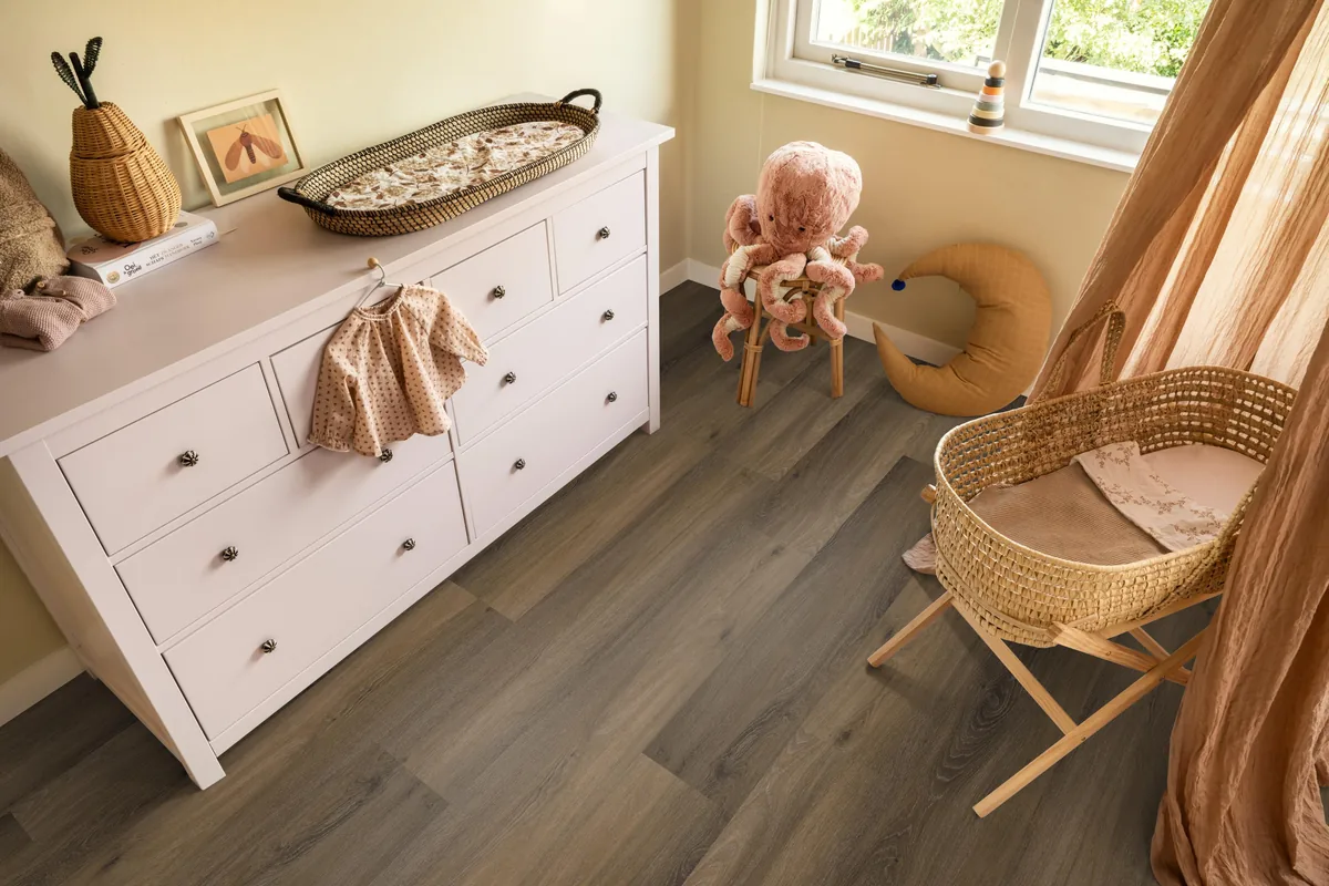 Paddington / Avanto Warm brown, klik pvc in een babykamer, met een witte commode en een rieten wieg