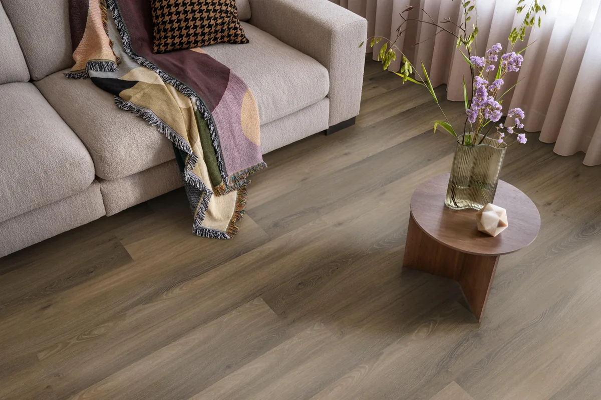 Paddington / Avanto Warm brown, klik pvc in een woonkamer, met een beige bank en een ronde bijzettafel met bloemen