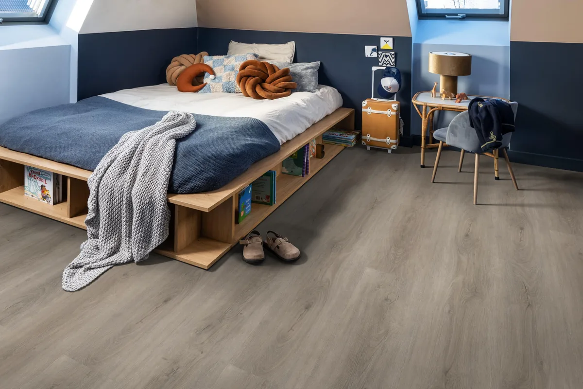Parramatta / Robusto Light Grey, klik pvc in een slaapkamer onder een schuin dak, met een houten bedombouw en sloffen ervoor