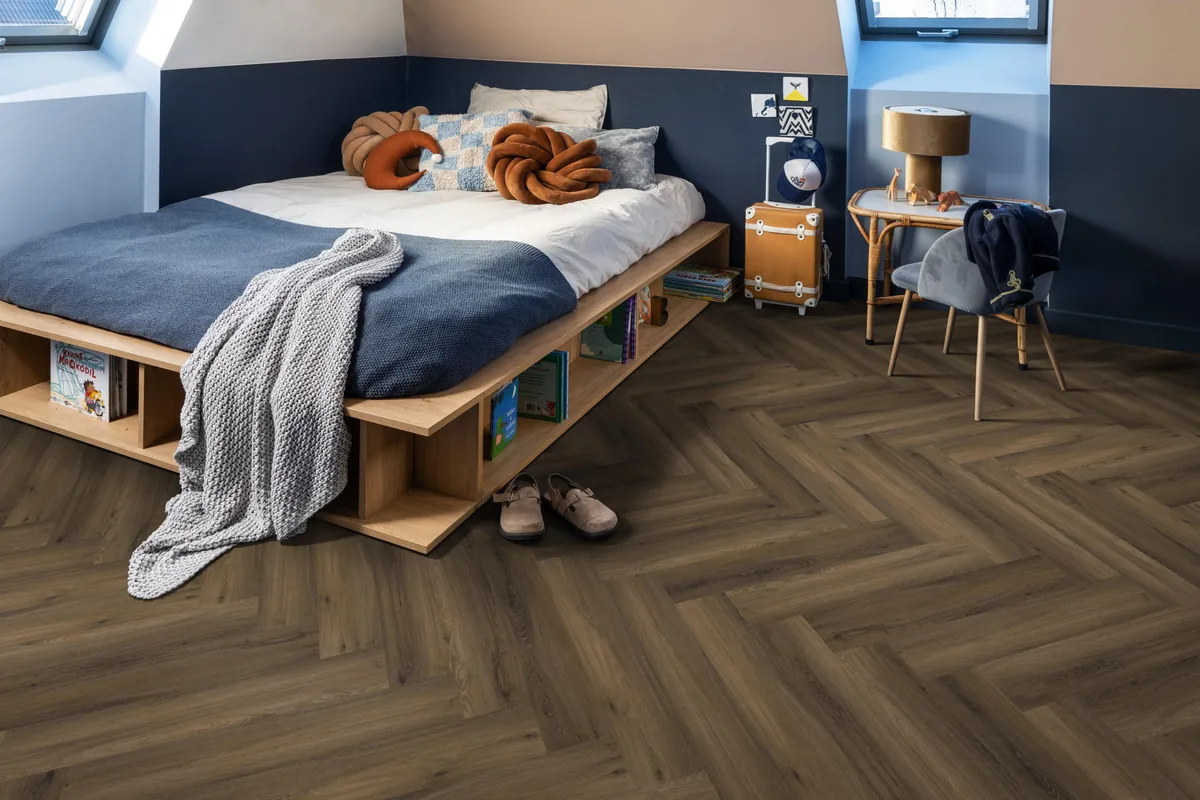 YUP / Spigato Warm brown, visgraat klik pvc in een slaapkamer onder een schuin dak, met een houten bedombouw en sloffen ervoor