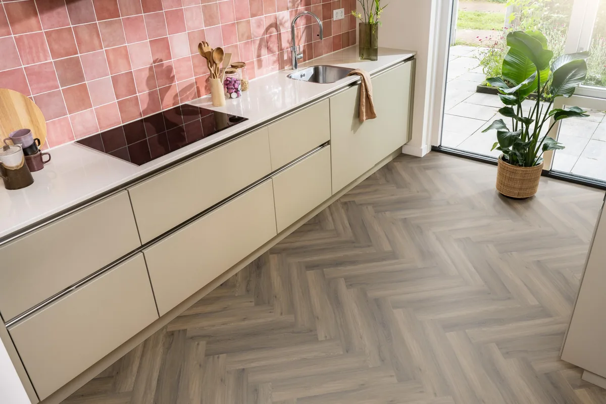 YUP / Spigato Warm brown, visgraat klik pvc in een keuken met een roze tegelwand en openslaande tuindeuren