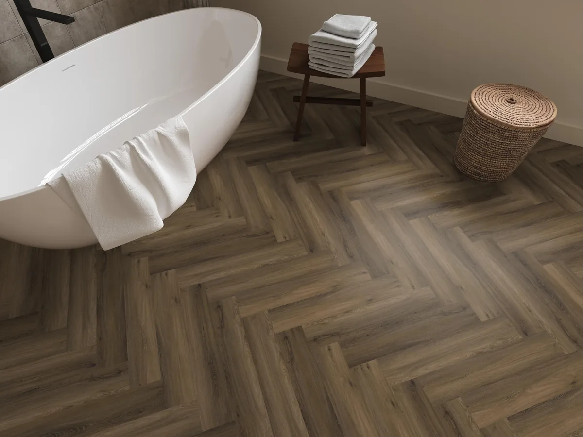 YUP / Spigato Warm brown, visgraat klik pvc in een badkamer, met een vrijstaand bad en een rieten wasmand