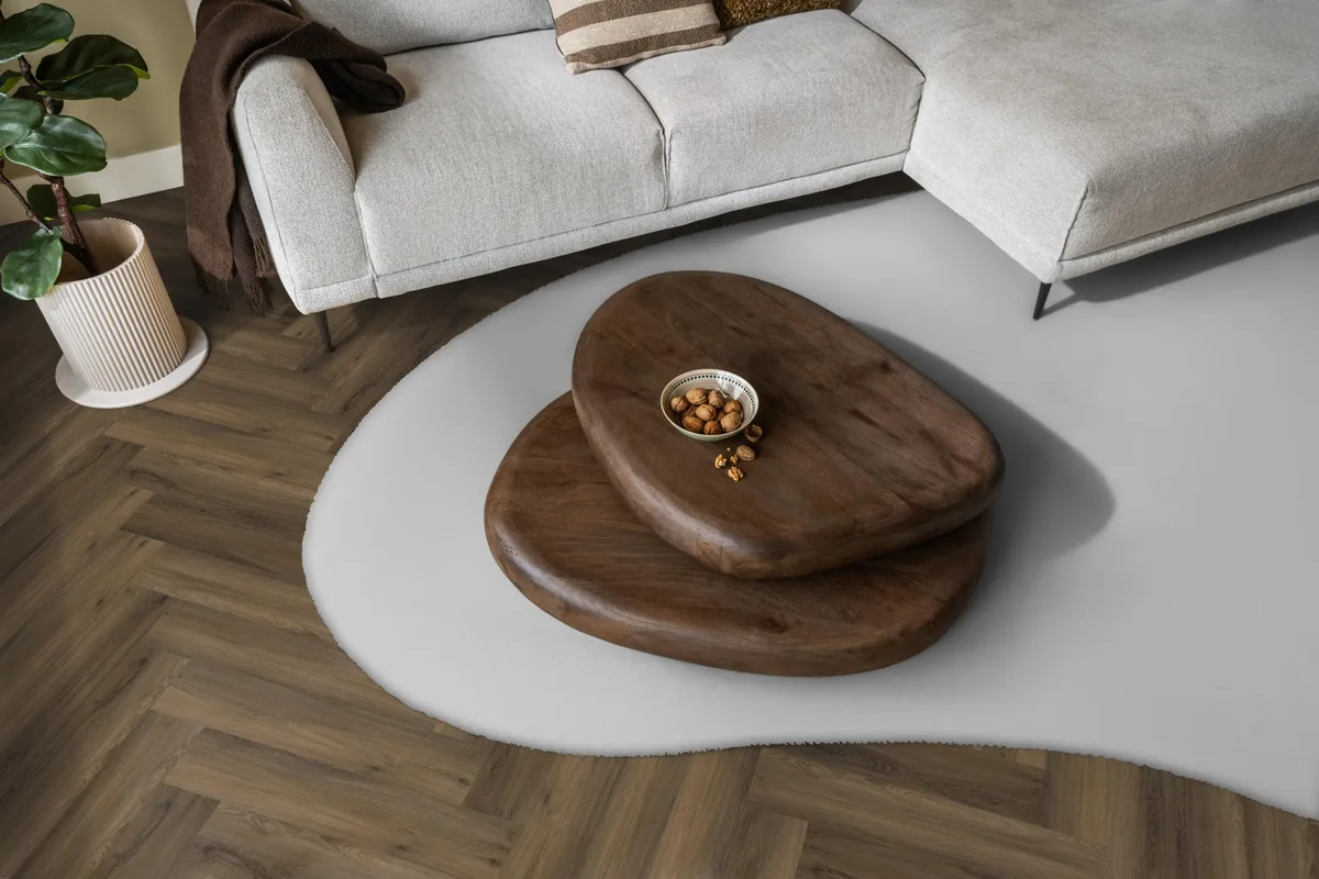 YUP / Spigato Warm brown, visgraat klik pvc in een woonkamer, met een lichte hoekbank en een wit vloerkleed