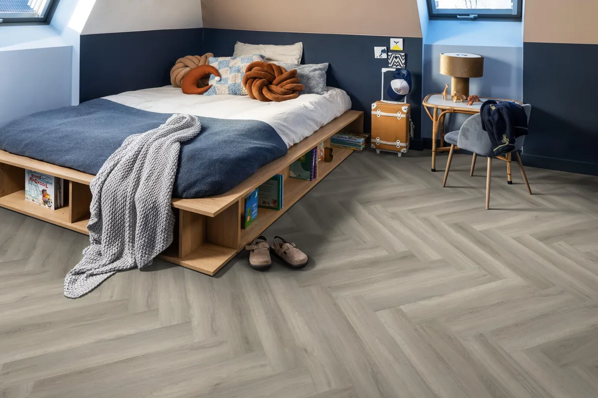 YUP / Spigato Grey, visgraat klik pvc in een slaapkamer onder een schuin dak, met een houten bedombouw en sloffen ervoor