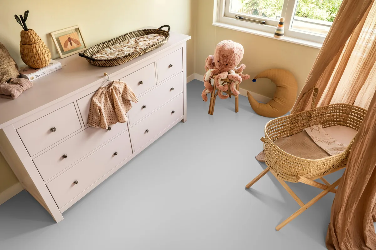 YUP / Spigato Grey, visgraat klik pvc in een babykamer, met een witte commode en een rieten wieg