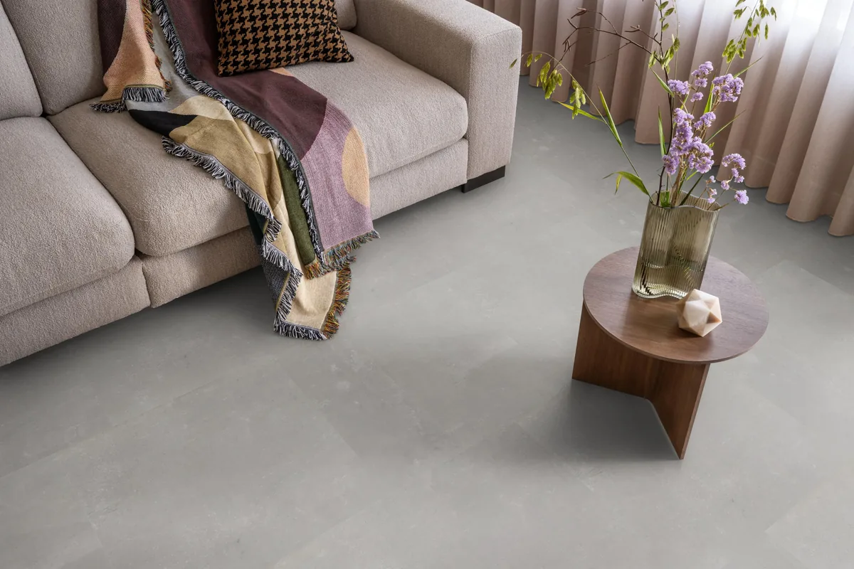 Victoria / Ceramo grey, klik pvc in een woonkamer, met een beige bank en een ronde bijzettafel met bloemen