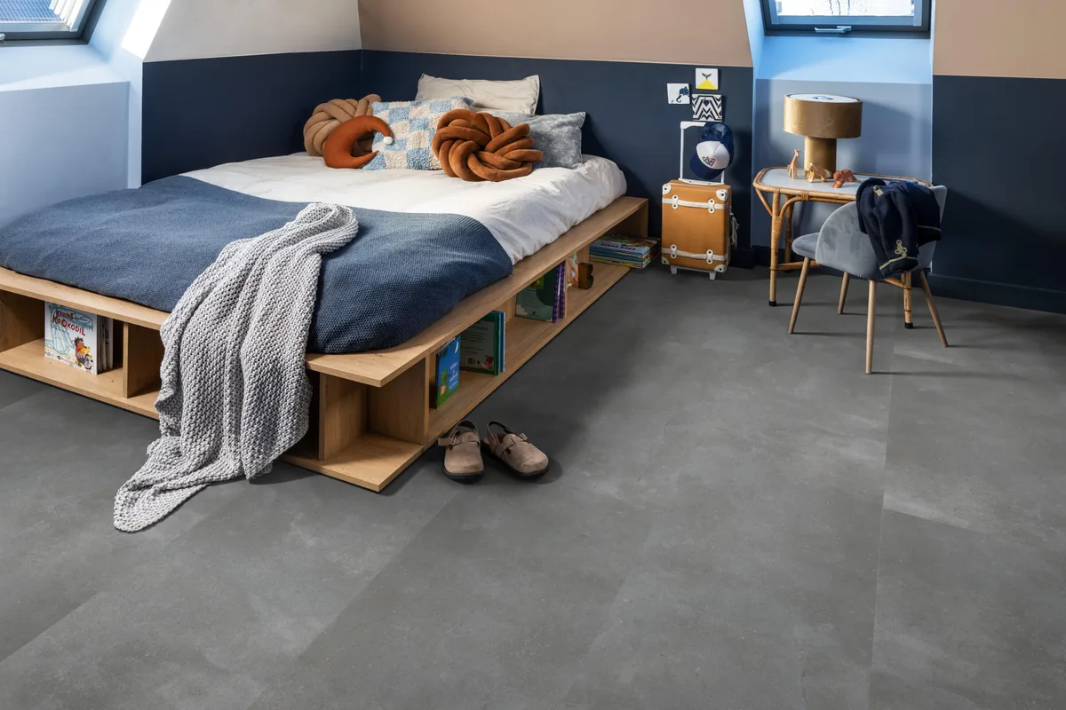 Ealing / Piazzo grey, klik pvc in een slaapkamer onder een schuin dak, met een houten bedombouw en sloffen ervoor