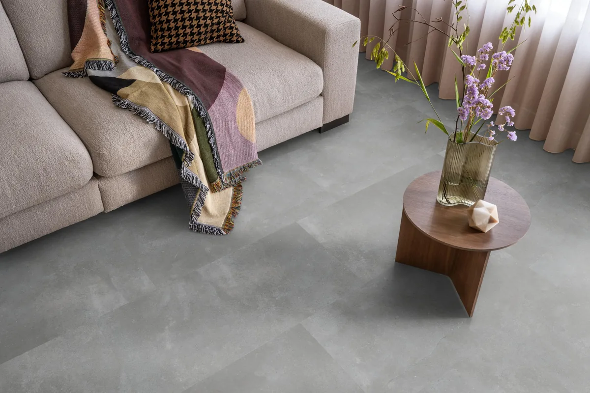 Ealing / Piazzo grey, klik pvc in een woonkamer, met een beige bank en een ronde bijzettafel met bloemen