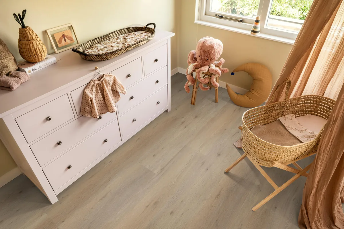 Leyton / Vivero natural oak, klik pvc in een babykamer, met een witte commode en een rieten wieg