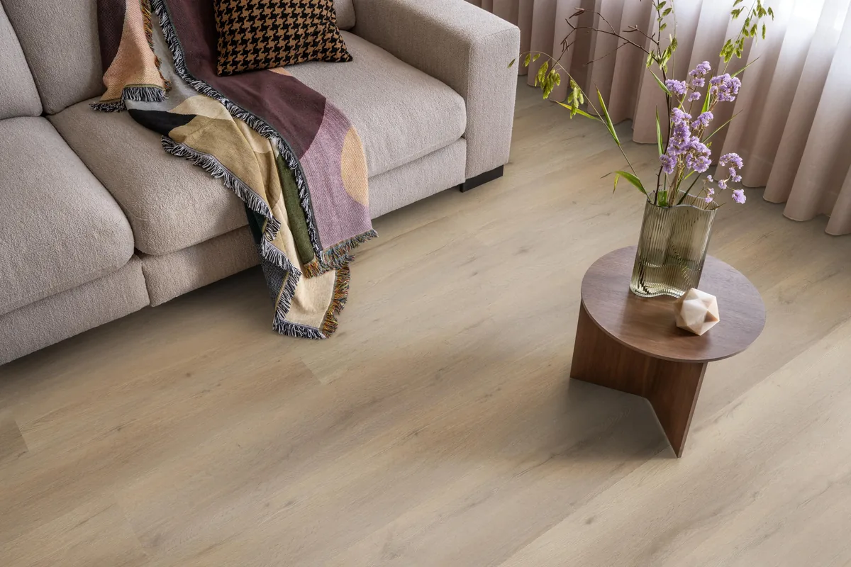 Leyton / Vivero natural oak, klik pvc in een woonkamer, met een beige bank en een ronde bijzettafel met bloemen