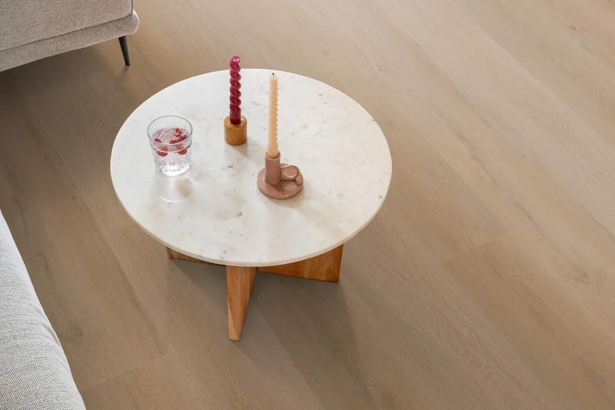 Leyton / Vivero warm oak, klik pvc in een woonkamer, met een ronde marmeren salontafel en twee kaarsen