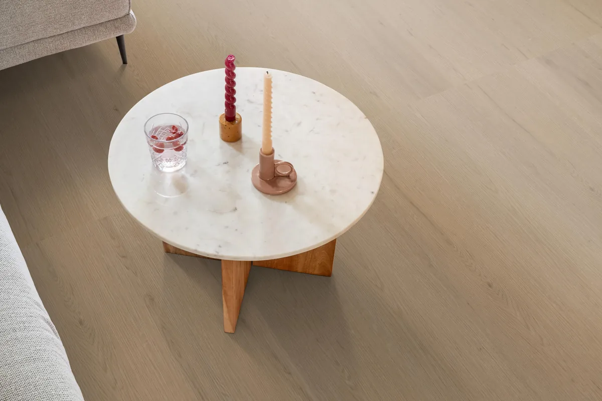 Barnet / Venera natural oak, klik pvc in een woonkamer, met een ronde marmeren salontafel en twee kaarsen