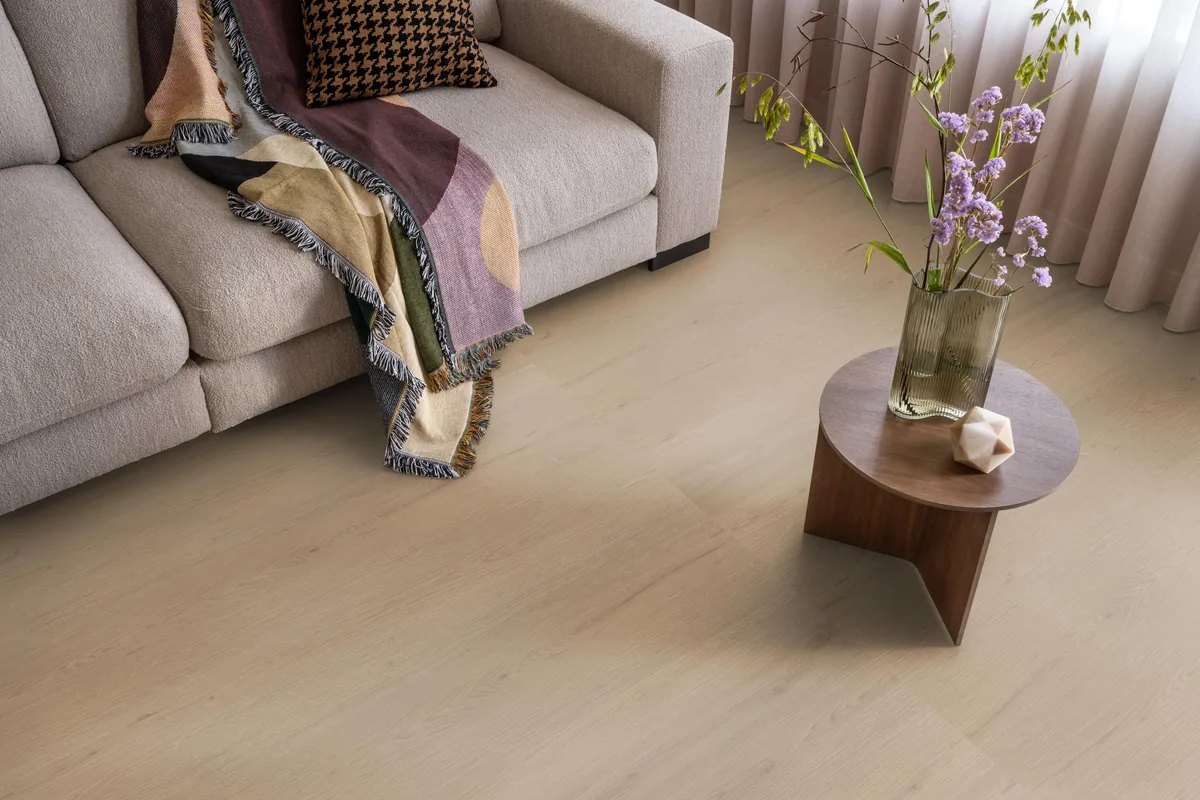 Barnet / Venera natural oak, klik pvc in een woonkamer, met een beige bank en een ronde bijzettafel met bloemen