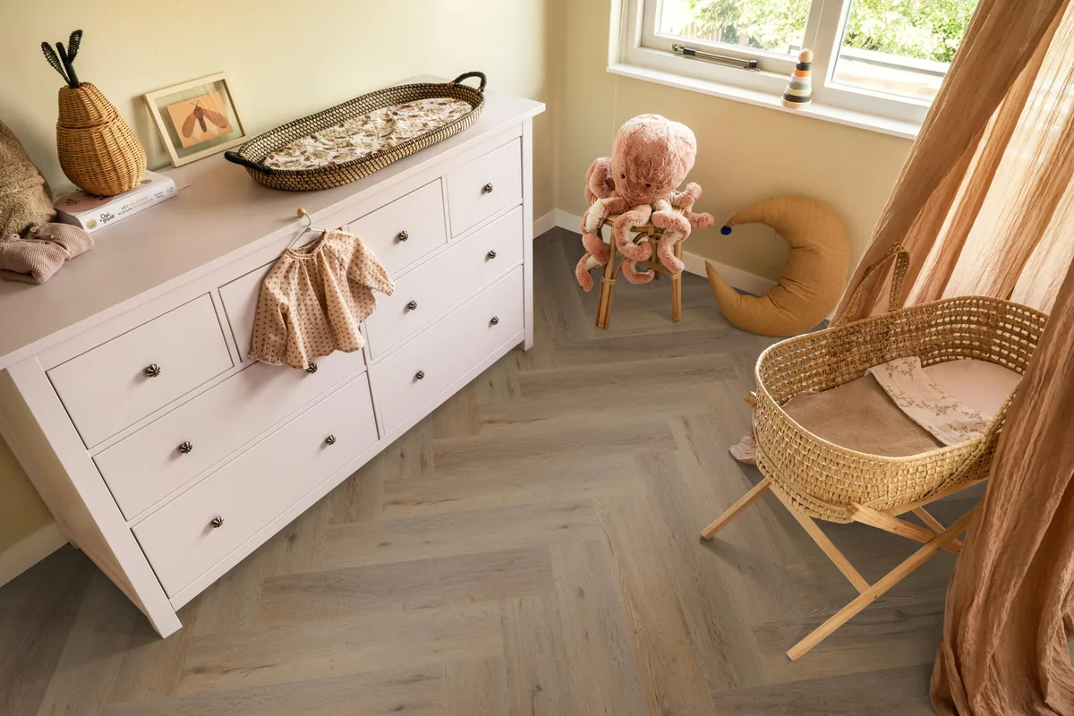Leyton / Vivero smoky, visgraat plak pvc in een babykamer, met een witte commode en een rieten wieg